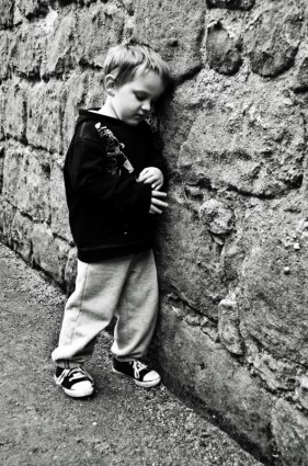 niño triste en un muro de piedra